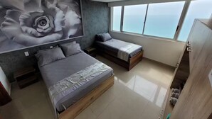 Quarto moderno com uma cama grande, uma cama menor e um sofá-cama. Há uma janela ampla com vista para o mar.