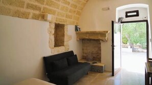 Une pièce avec une cheminée en pierre, un canapé noir et une porte donnant sur l’extérieur.