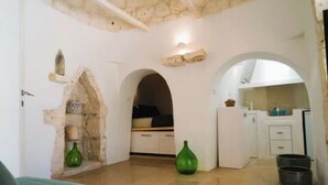 Une pièce avec un mur en pierre, un vase vert et un coin cuisine avec des meubles blancs.