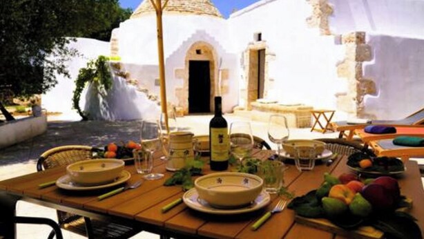 Une table à manger installée à l’extérieur, avec un bâtiment blanc en arrière-plan.