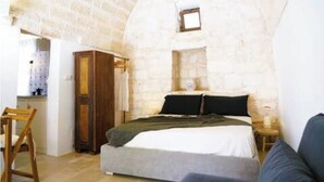 Une chambre avec un mur en pierre, un lit, une armoire en bois et une petite table avec une lampe.