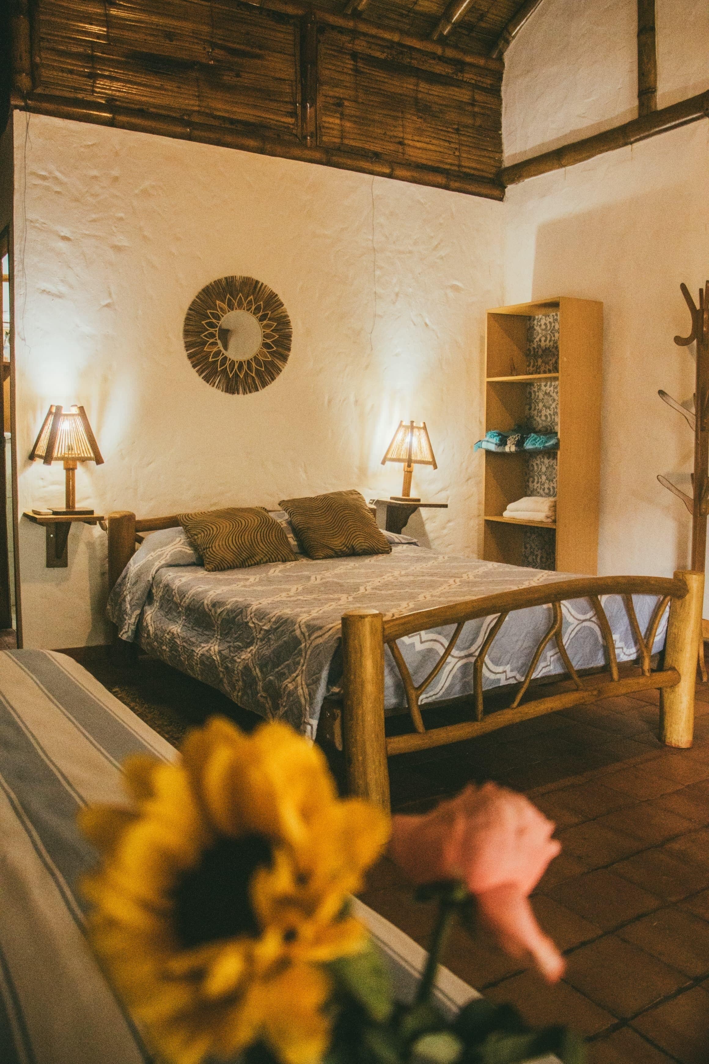 Een slaapkamer met een houten bed, twee bedlampen, een wandspiegel en een inbouwplank met opgevouwen handdoeken.