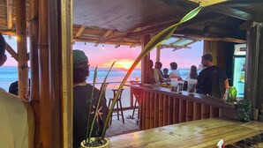 A wooden bar area with a view of the sunset over the ocean, a potted plant, and a bottle of water on the counter. - HOSTAL ROSA MISTICA  (Montañita)