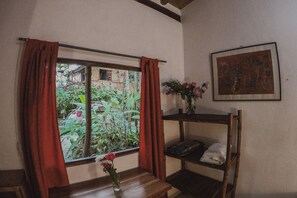 A room with a window, a wooden bench, a small table with a vase, a shelf with a painting, and a bunk bed.