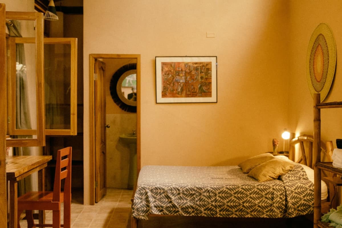 Un dormitorio con cama, muebles de madera, una lámpara colgante y un cuadro en la pared.