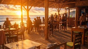 An outdoor dining area with wooden tables and benches, overlooking the ocean at sunset. - HOSTAL ROSA MISTICA  (Montañita)