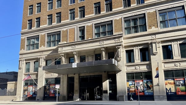 A multi-story building with a prominent entrance, large windows, and a flag. - Luxury Downtown Apt with Parking, Gym, and Lap Pool · Sleeps 4-5 (Milwaukee)
