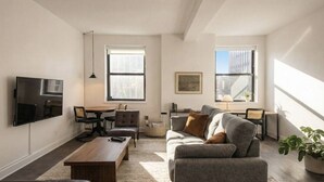 A modern living room with a sofa, coffee table, and TV. There are windows, a painting, and a plant. - Luxury Downtown Apt with Parking, Gym, and Lap Pool · Sleeps 4-5 (Milwaukee)
