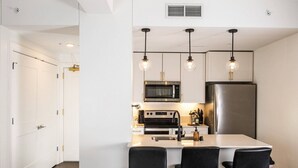 A modern kitchen with a microwave, oven, and refrigerator, a bar area with stools, and pendant lighting. - Luxury Downtown Apt with Parking, Gym, and Lap Pool · Sleeps 4-5 (Milwaukee)