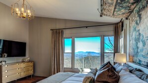 Un dormitorio con una cama grande, un televisor y vistas a las montañas desde la ventana.