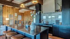 Una cocina moderna con detalles de madera, una isla central, taburetes de bar y electrodomésticos integrados.