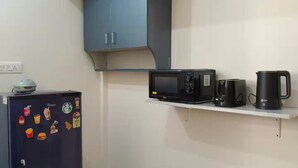 Une cuisine compacte équipée d’un réfrigérateur, d’un four à micro-ondes, d’une machine à café et d’une bouilloire, le tout placé sur une étagère blanche.