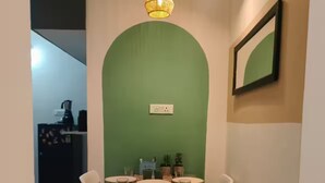 Un coin repas agrémenté d’un mur d’accent vert, de chaises blanches et d’une table dressée pour quatre personnes.