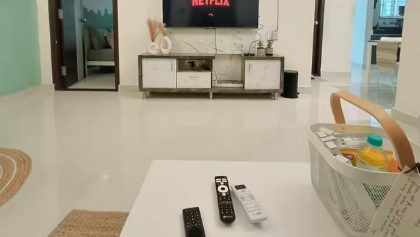 Un salon avec un téléviseur à écran plat fixé au mur, une table basse blanche et un panier rempli d’objets divers.
