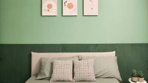 Un lit avec une tête de lit verte, deux coussins à motifs et trois œuvres d’art accrochées au mur au-dessus.