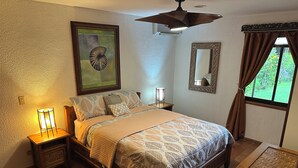 A bedroom with a bed, bedside lamps, a ceiling fan, a framed artwork, a mirror, and a window with curtains. - Riverside oasis with private pool and backyard.  Walking distance to the beach. (Paquera)