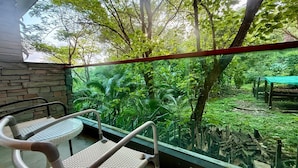 A balcony with wicker chairs and a table, overlooking a lush garden with various plants and trees. - Emerald 412a - Studio With Balcony and Shared Pool (Patong)