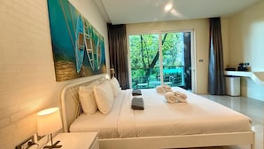 A hotel room with a large bed, a painting on the wall, and a view of greenery through the window. - Emerald 412a - Studio With Balcony and Shared Pool (Patong)