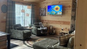 Ein gemütliches Blockhaus-Interieur mit Holzwänden, einem an der Wand befestigten Fernseher, einem Kamin und einer bequemen Sitzecke.
