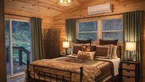 Ein Schlafzimmer einer Holzhütte mit einem Bett, zwei Nachttischen, einem Fenster und Blick ins Freie.