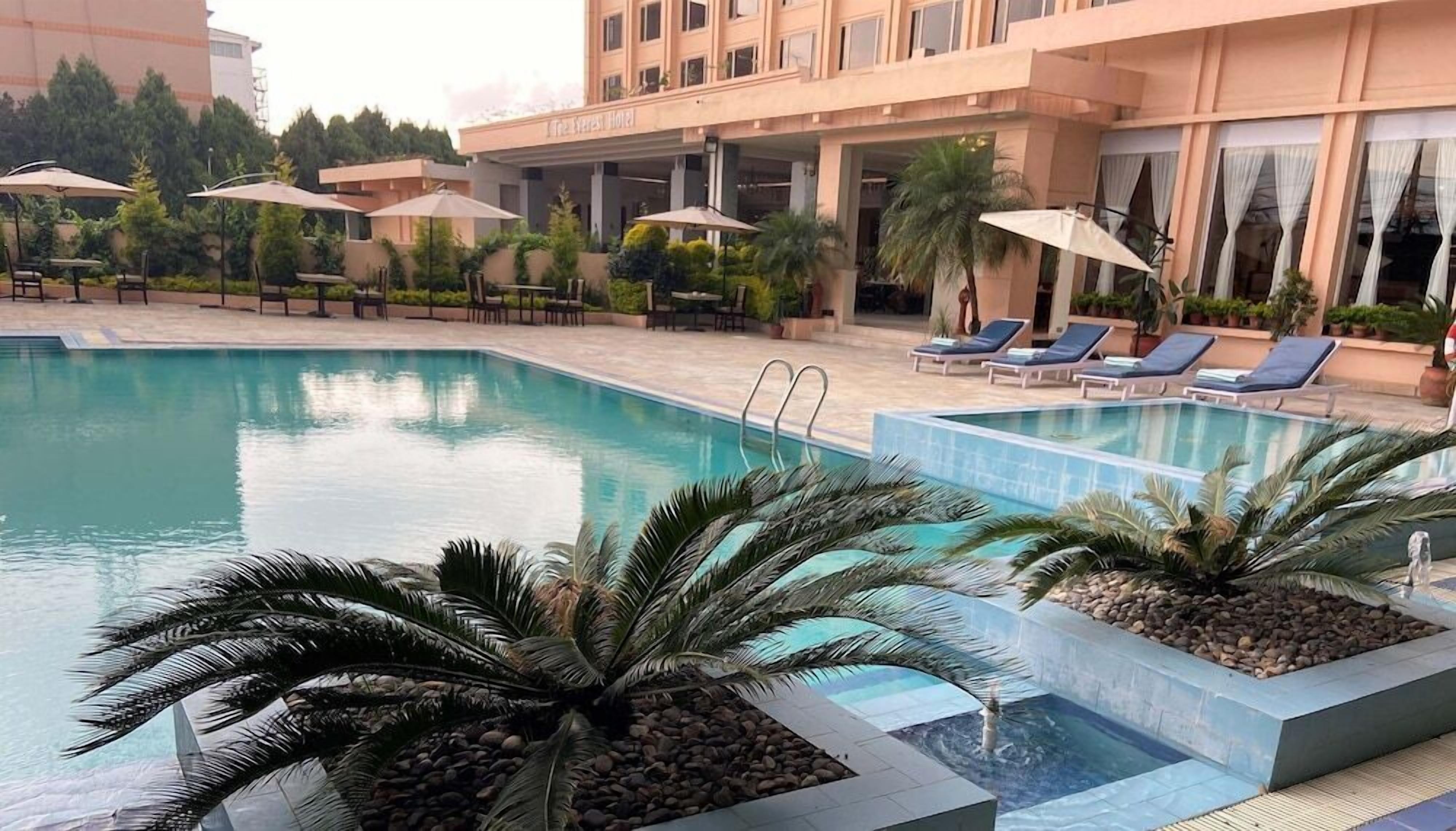 A hotel pool area with lounge chairs and umbrellas, surrounded by palm trees and a building with a sign that reads "The Express Hotel".