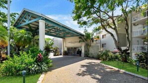 A resort entrance with a covered walkway, palm trees, and a building labeled "Caribbean Beach Resort". - Coconut Vibes- Overlooking Resort Pool Ocean Glimpses, Holloways Beach - Cairns (Holloways Beach)