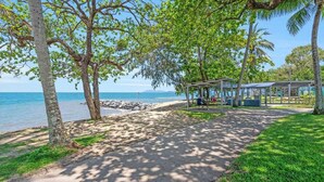 A coastal park with a paved walkway, picnic tables, and a covered seating area by the beach. - Coconut Vibes- Overlooking Resort Pool Ocean Glimpses, Holloways Beach - Cairns (Holloways Beach)