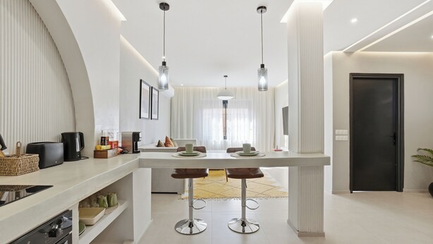 Uma cozinha moderna com uma ilha central, banquetas de bar e um espaço de refeições com mesa e cadeiras.