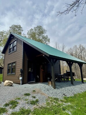 A two-story cabin with a covered outdoor seating area and a gravel driveway.