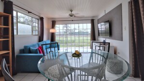 A modern living room with a glass dining table, blue sofa, and a TV mounted on the wall. - LIMITED OFFER FOR FIRST GUESTS - ENJOY MY HOME AT A GREAT RATE! (Noord,)