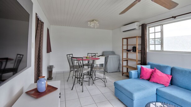 A room with a blue sofa, a dining table with chairs, a ceiling fan, and a window with a view. - LIMITED OFFER FOR FIRST GUESTS - ENJOY MY HOME AT A GREAT RATE! (Noord,)