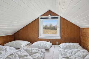 Ein Schlafzimmer mit Schrägdach, einem Fenster mit Blick auf ein Feld und zwei Betten mit weißer Bettwäsche.