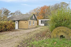 A small brick building with a sloped roof, a small attached structure, and a large circular object with 'BROHUS' inscribed on it. - Cozy little holiday oasis in beautiful nature (Bækmarksbro)