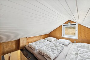 A small, cozy room with a sloped ceiling, a window with a view of a field, and a bed with white bedding. - Cozy little holiday oasis in beautiful nature (Bækmarksbro)