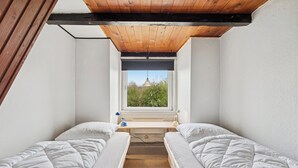 Ein kleines Zimmer mit zwei Betten, einem Fenster und einem Schreibtisch.