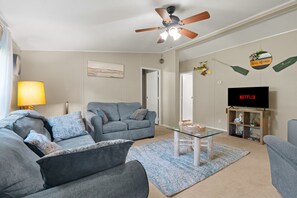 A living room with a grey sofa set, a glass coffee table, a ceiling fan, and a television on a wooden stand. - Lake Escape Cottage | Lake Access w/ Fire Pit! (Coldwater)