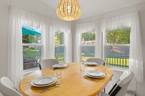 A dining area with a round table set for four, white chairs, and a hanging light fixture. - Lake Escape Cottage | Lake Access w/ Fire Pit! (Coldwater)
