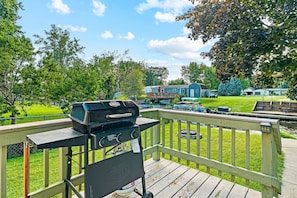 A deck with a barbecue grill, a view of a residential area, and a body of water.