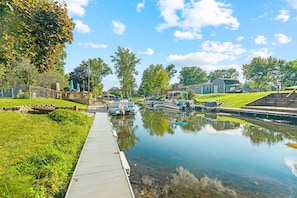 A canal with boats, a wooden dock, and a grassy area with trees.