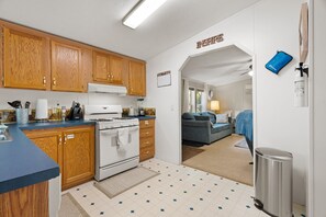 A kitchen with wooden cabinets, a stove, and a blue countertop. - Lake Escape Cottage | Lake Access w/ Fire Pit! (Coldwater)