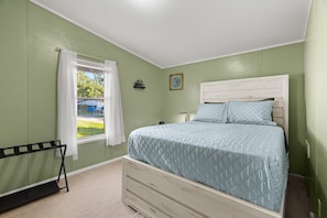 A bedroom with a bed, a window with curtains, a small shelf with a bicycle, and a picture on the wall.