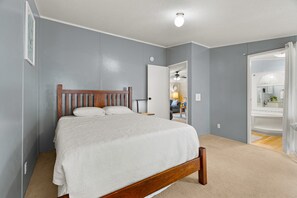 A bedroom with a wooden bed, a ceiling fan, and a bathroom visible through an open door. - Lake Escape Cottage | Lake Access w/ Fire Pit! (Coldwater)
