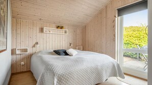 A bedroom with a large bed, wooden walls, a window, and a small shelf with decorative items. - Nice home in Tarm with sauna (Tarm)