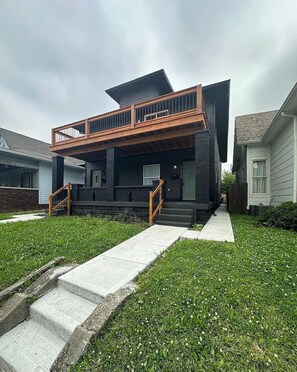 A modern two-story house with a balcony, a front porch, and a well-maintained lawn.