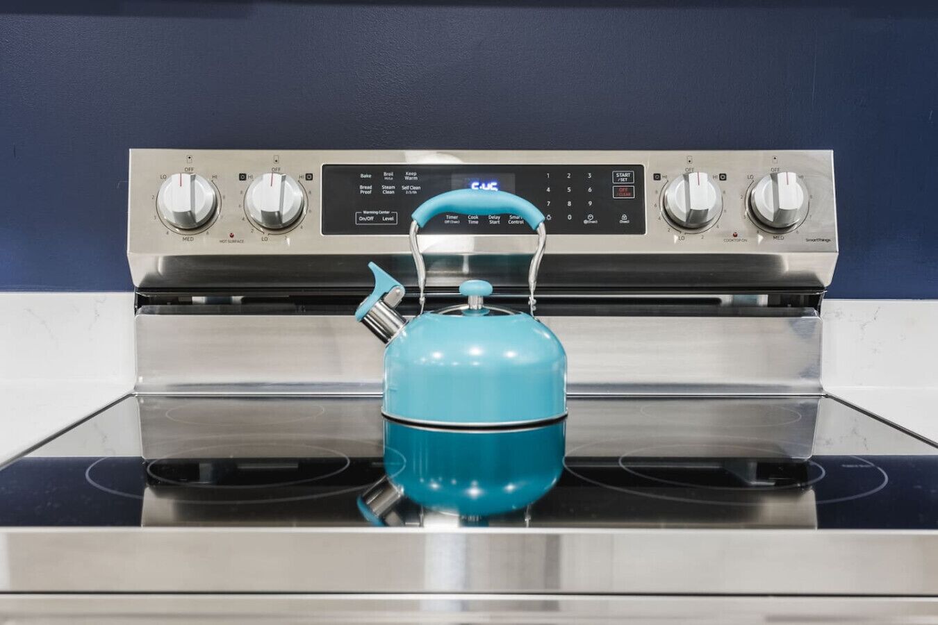 A kitchen with a stainless steel stove and a teal kettle on the stovetop.