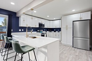 Een moderne keuken met witte kasten, roestvrijstalen apparatuur en een centraal eiland met barstoelen.