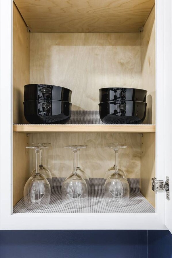 A cabinet with two shelves; the top shelf holds black containers, and the bottom shelf has three clear wine glasses.