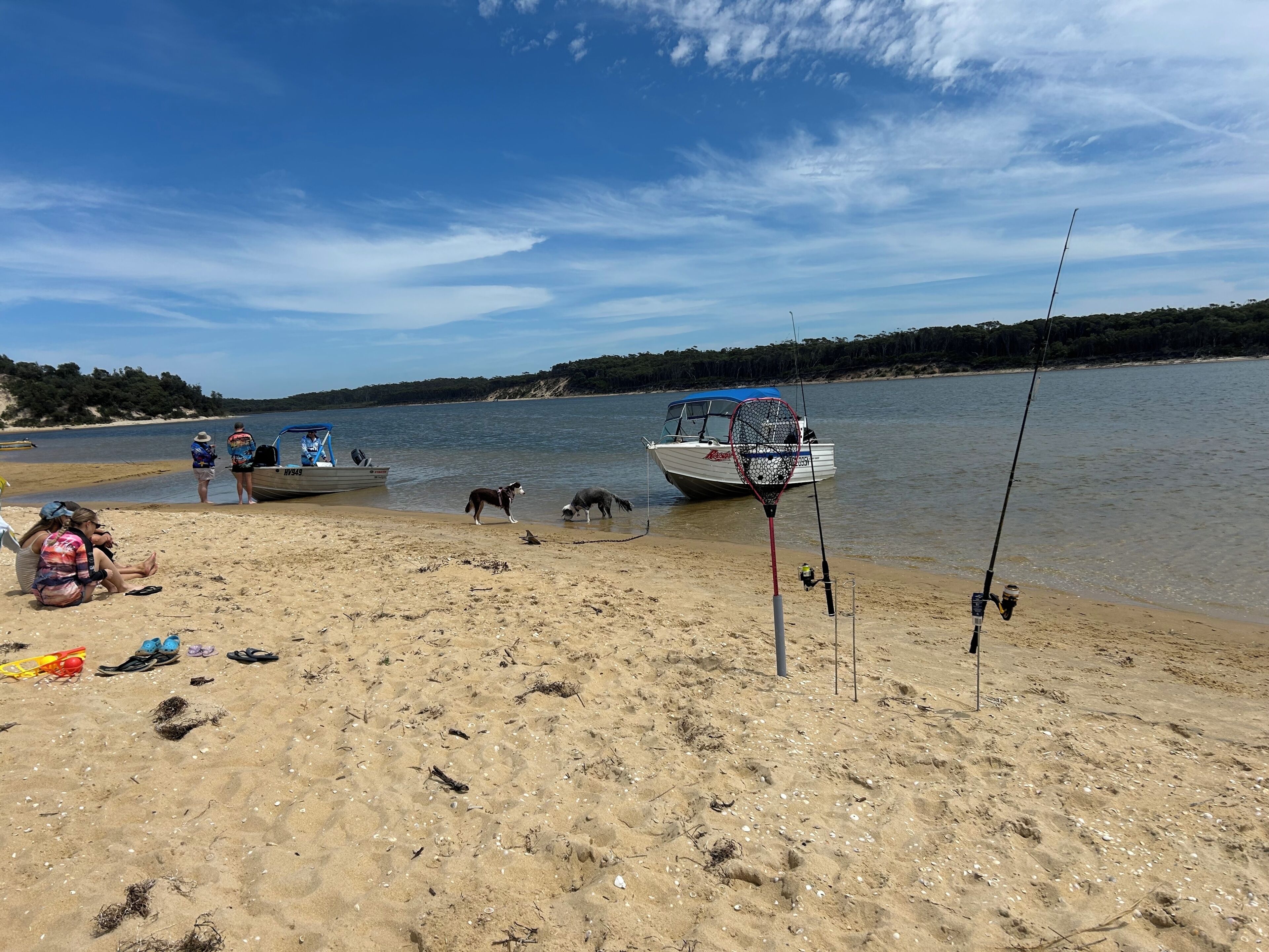 A beach with boats, fishing rods, and people.