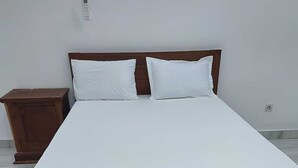 Een houten bed met witte beddengoed in een kamer met betegelde vloer.