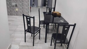 Een eethoek met een zwarte tafel en stoelen, een stenen muur en uitzicht op een kamer met gordijnen.